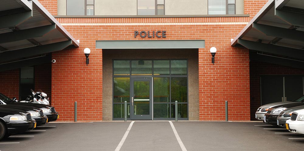 The front door of a police station, with the front of a few police cars and a couple of police motorcycles visible off to the side